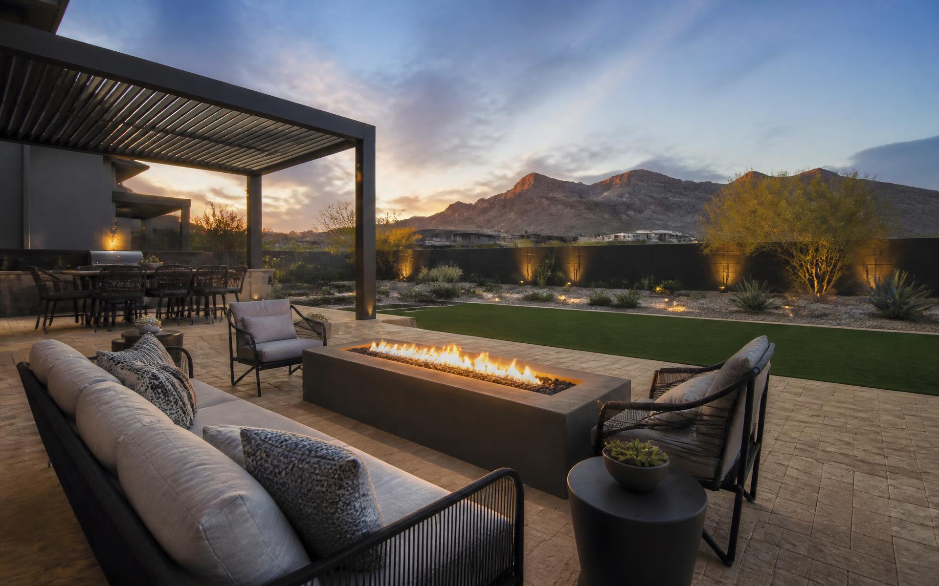 Upscale Las Vegas desert backyard at dusk with paver patio, linear fire table, pergola and artificial turf